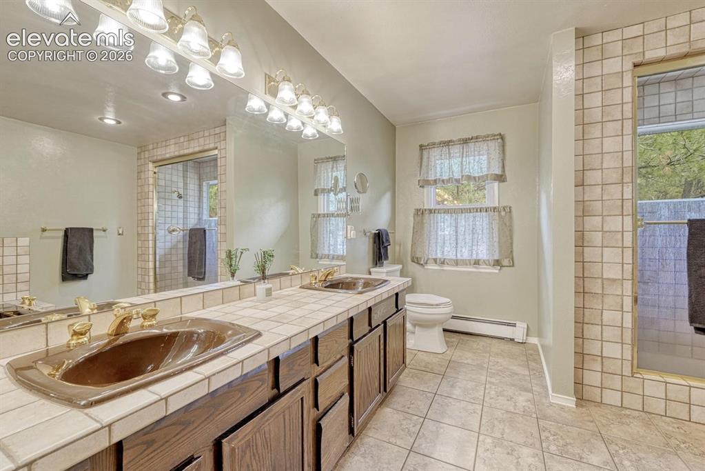 Image 26 of 48: Dual vanity featuring tile countertops and integrated sinks with brass-fini