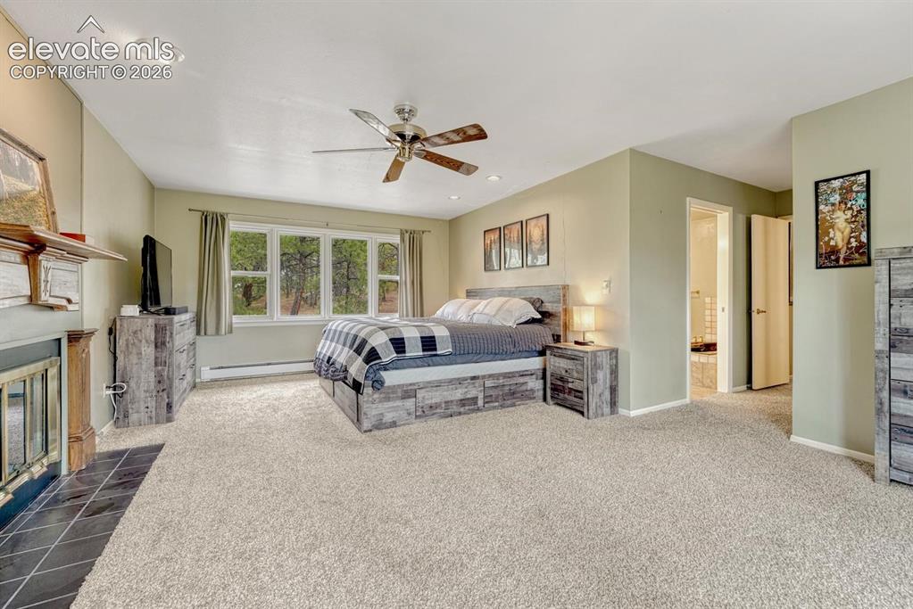 Image 29 of 48: Spacious carpeted room featuring a large window, ceiling fan, and a firepla