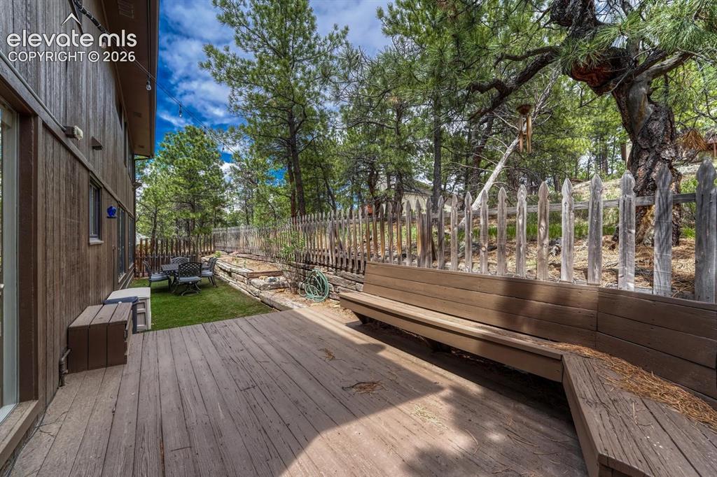 Image 35 of 48: Spacious wooden deck with built-in bench seating, bordered by a privacy fen