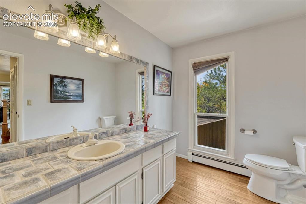 Image 9 of 48: Bathroom featuring a full-width vanity mirror, tile countertop, and white c
