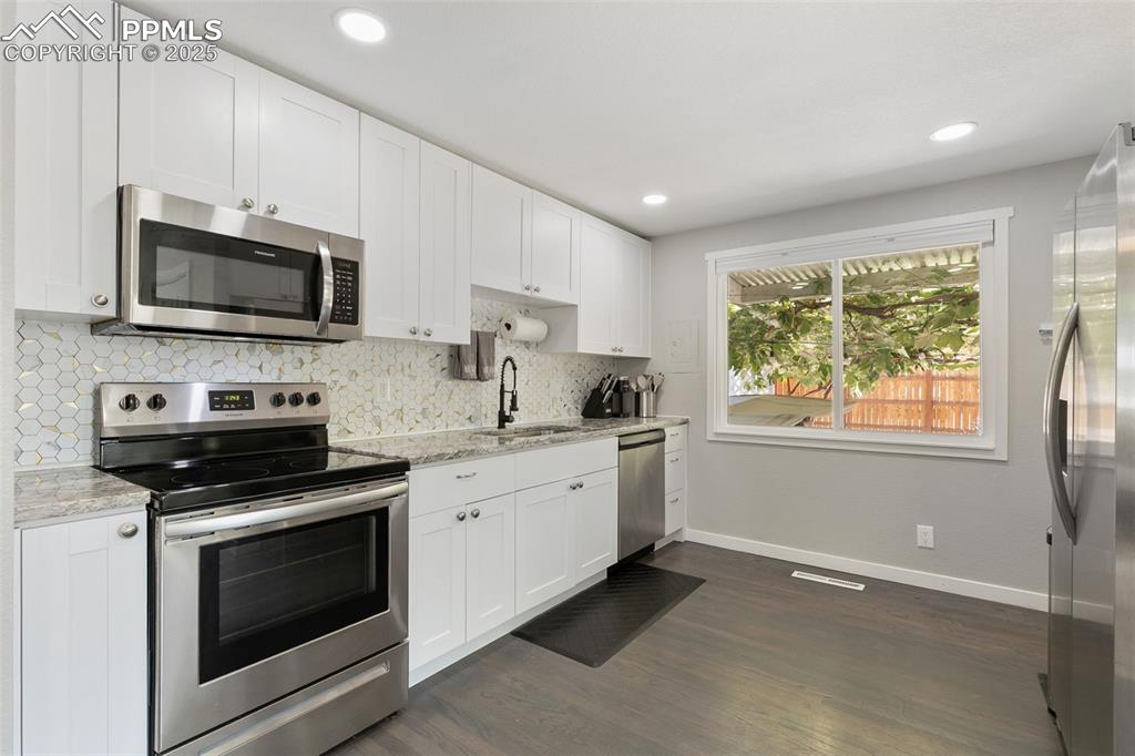 Image 9 of 39: Kitchen with stainless steel appliances, tasteful backsplash, light stone c