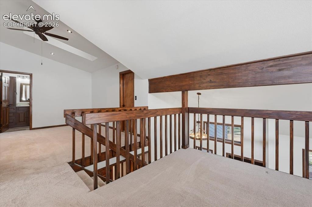 Image 20 of 46: Carpeted loft area featuring wood railings, vaulted ceiling, ceiling fan, a