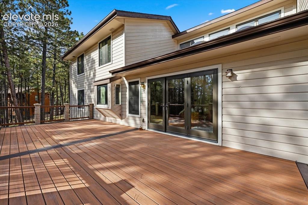 Image 38 of 46: Expansive wood-finish deck with dark railing and stone-clad pillars