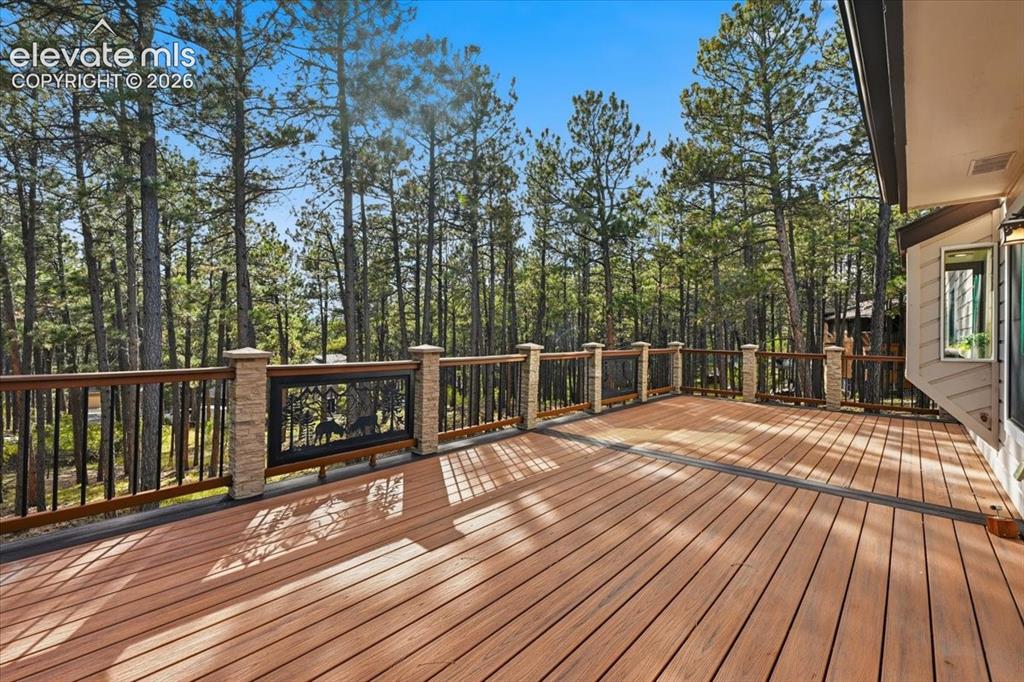 Image 39 of 46: Expansive wood-finish deck with decorative metal railing panels and stone-w