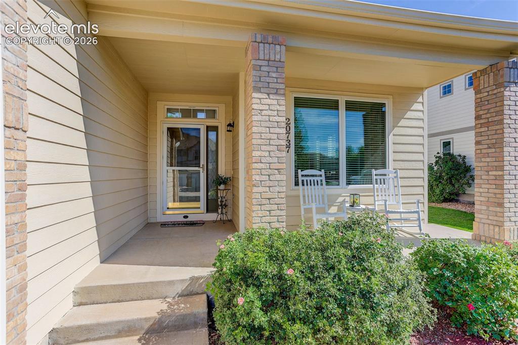 Image 2 of 42: Covered concrete porch with brick columns, siding exterior, and mature land
