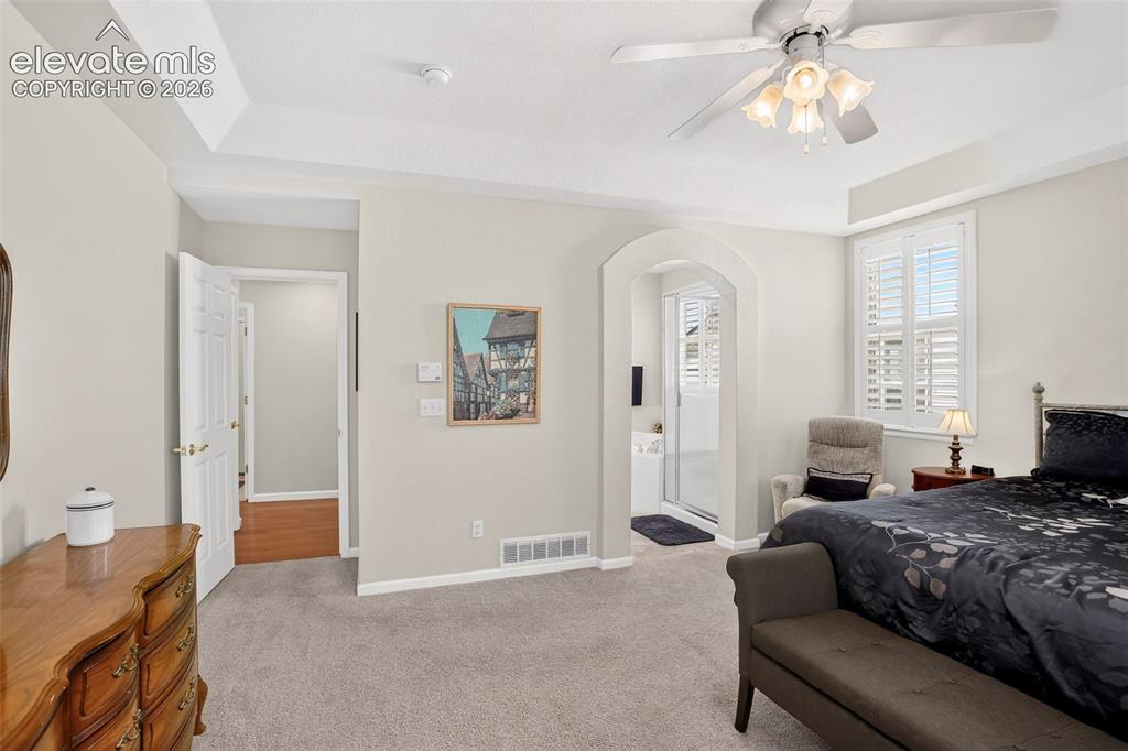 Image 23 of 42: Tray ceiling with a ceiling fan light fixture, arched doorway, and plantati