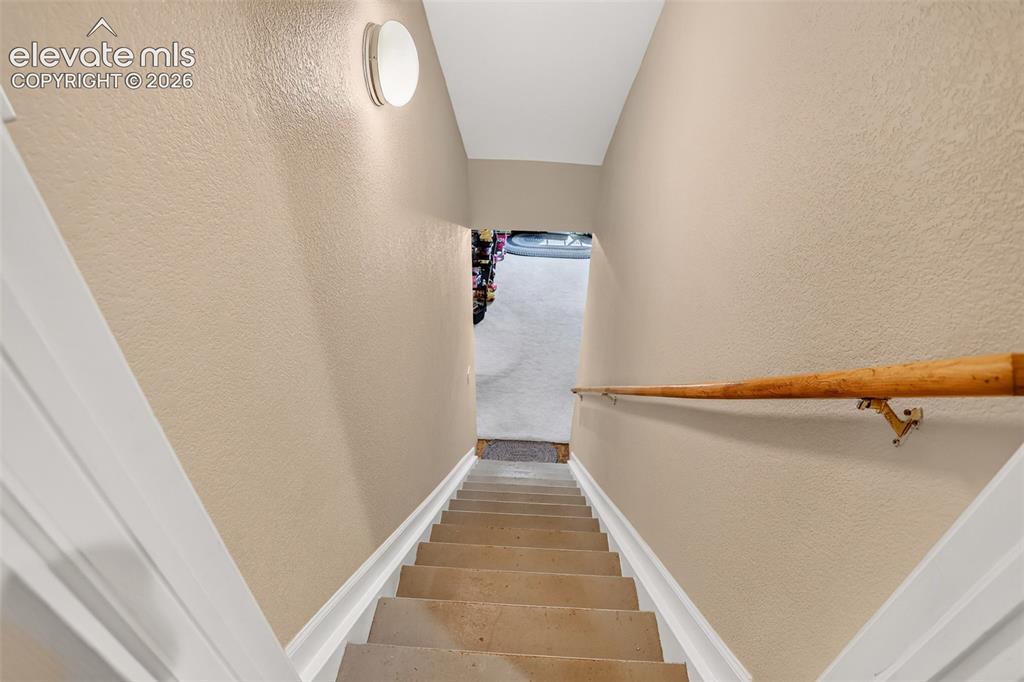 Image 34 of 42: Staircase going to basement with light beige textured walls, white trim, wo