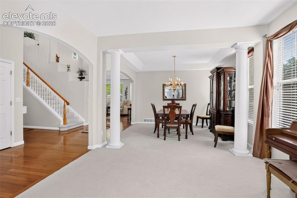 Image 8 of 42: Arched doorway, wood flooring, carpeted stairs with wood handrail, columns,