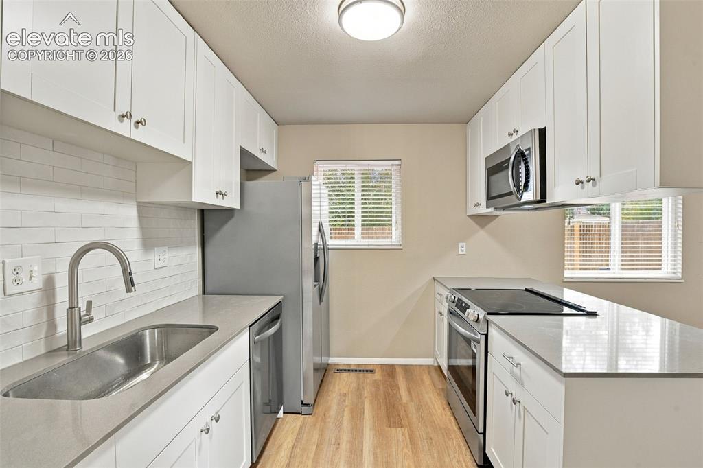 Image 12 of 50: Kitchen featuring white cabinetry, solid-surface countertops, horizontal ti