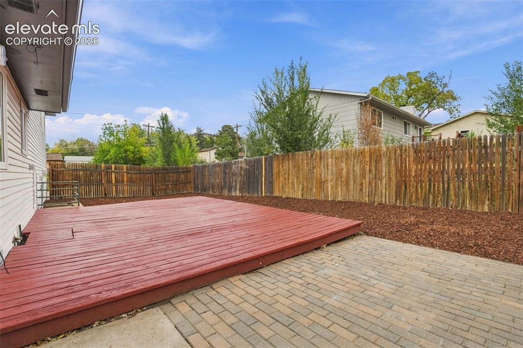 Image 28 of 50: Outdoor living area featuring a wood deck, stone-paver patio, wood-slat per