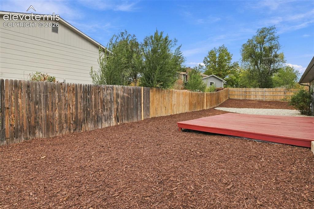 Image 31 of 50: Backyard featuring a red-painted wood deck, mulch ground cover, and a wood 