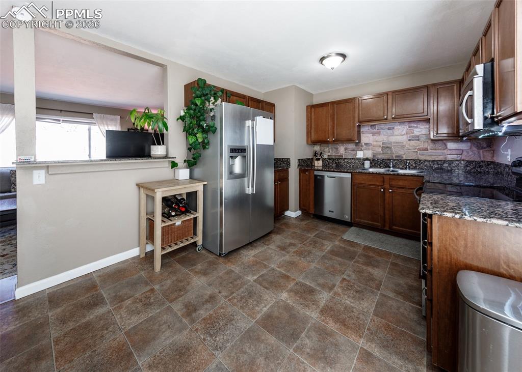 Image 14 of 39: Kitchen with stone finish floors, stainless steel appliances, dark stone co