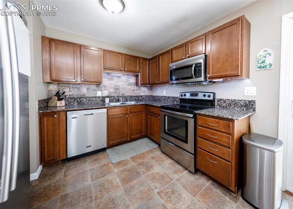 Image 15 of 39: Kitchen featuring stainless steel appliances, dark stone countertops, wood 