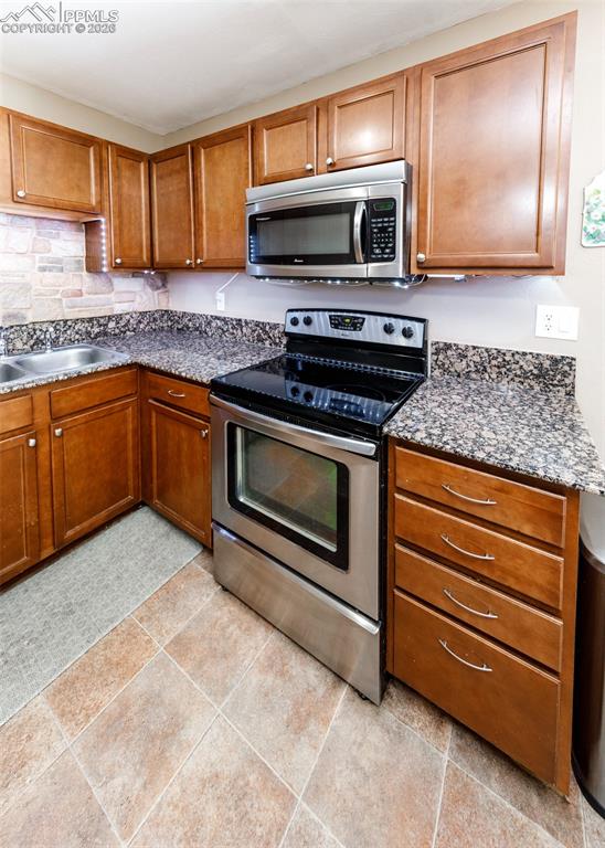 Image 17 of 39: Kitchen with stainless steel appliances, wood finish cabinetry, and dark st