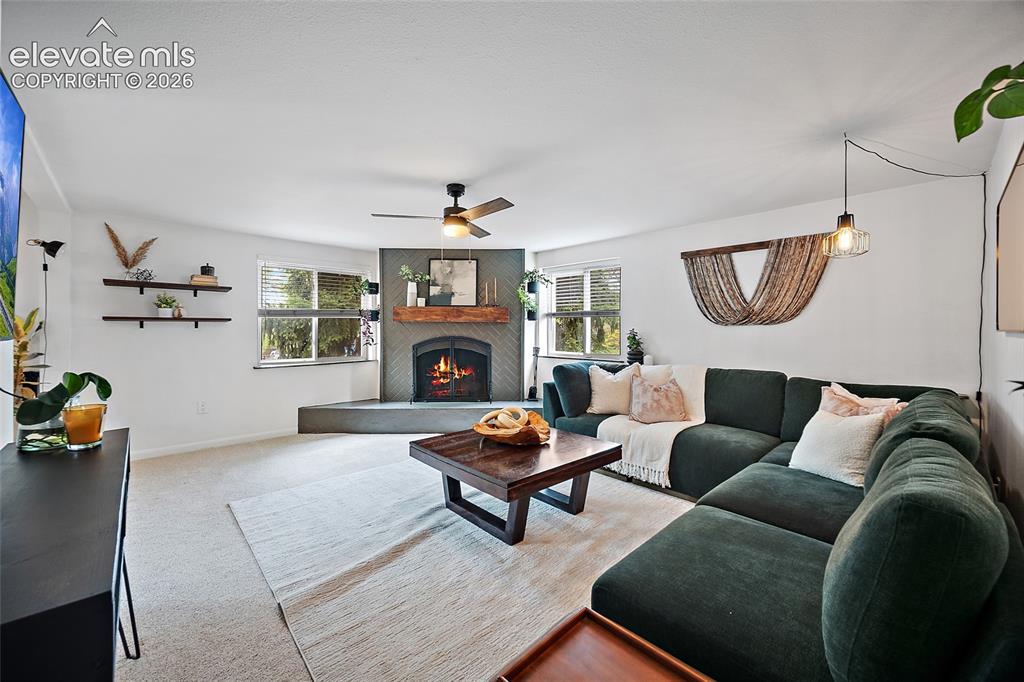 Image 19 of 43: Living area featuring a corner fireplace with a wood mantel, a ceiling fan,