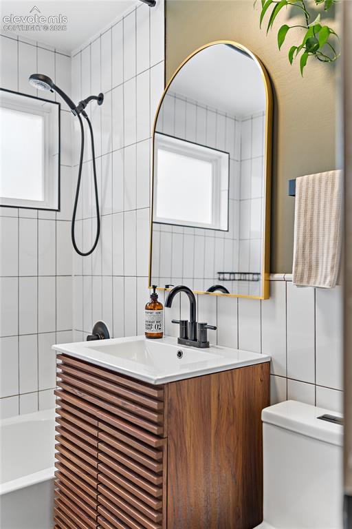 Image 30 of 43: Bathroom featuring a wood-finish vanity with louvered doors, a white integr
