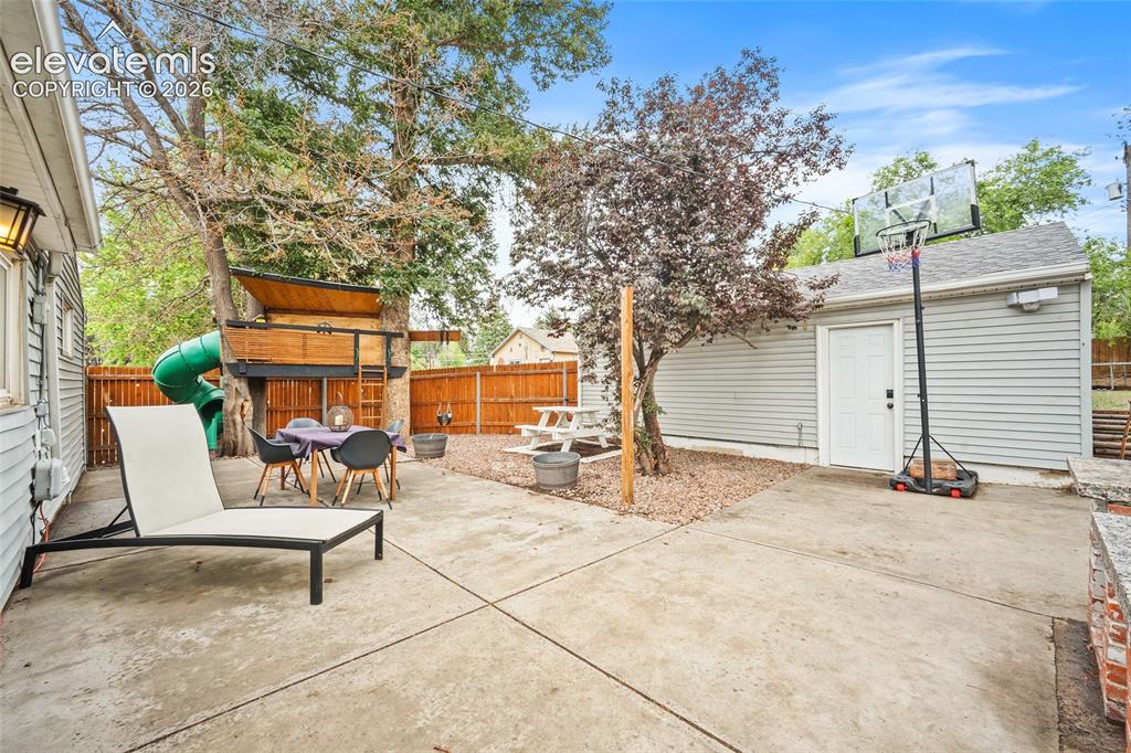 Image 38 of 43: Spacious concrete patio with a built-in treehouse featuring a slide, a deta