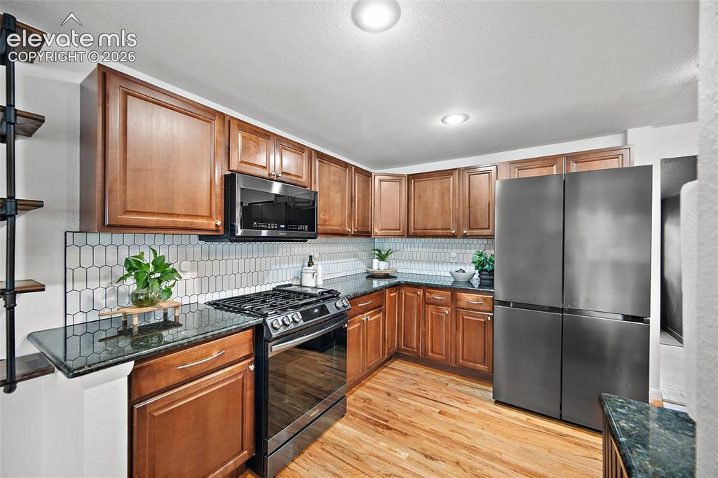Image 9 of 43: Kitchen featuring wood-finish flooring, dark stone countertops, and a white