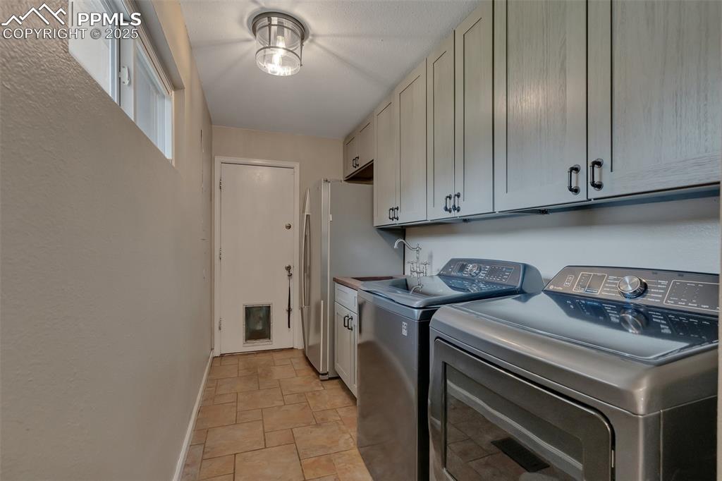 Image 24 of 41: Washroom with cabinet space, washer and dryer, and light stone finish floor
