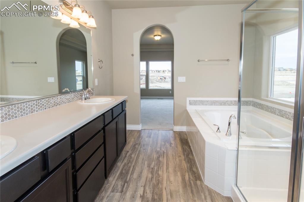 Image 20 of 28: Full bath with wood finished floors, double vanity, a sink, a bath, and dec