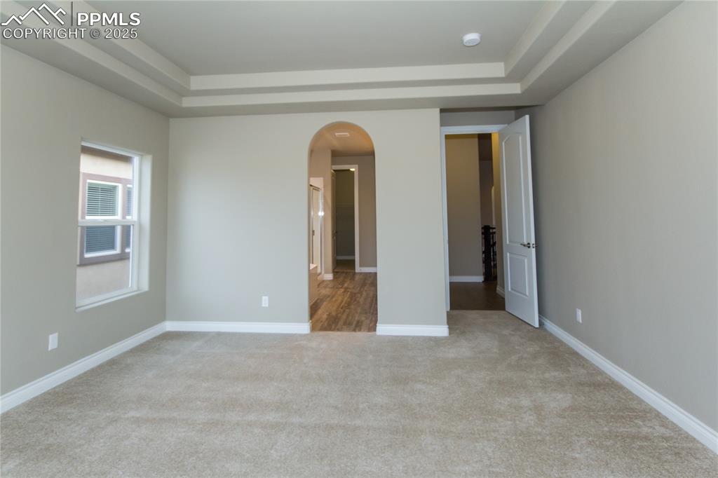 Image 22 of 28: Unfurnished room with arched walkways, a raised ceiling, carpet floors, and