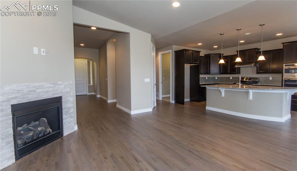 Image 5 of 28: Kitchen featuring dark brown cabinetry, under cabinet range hood, arched wa