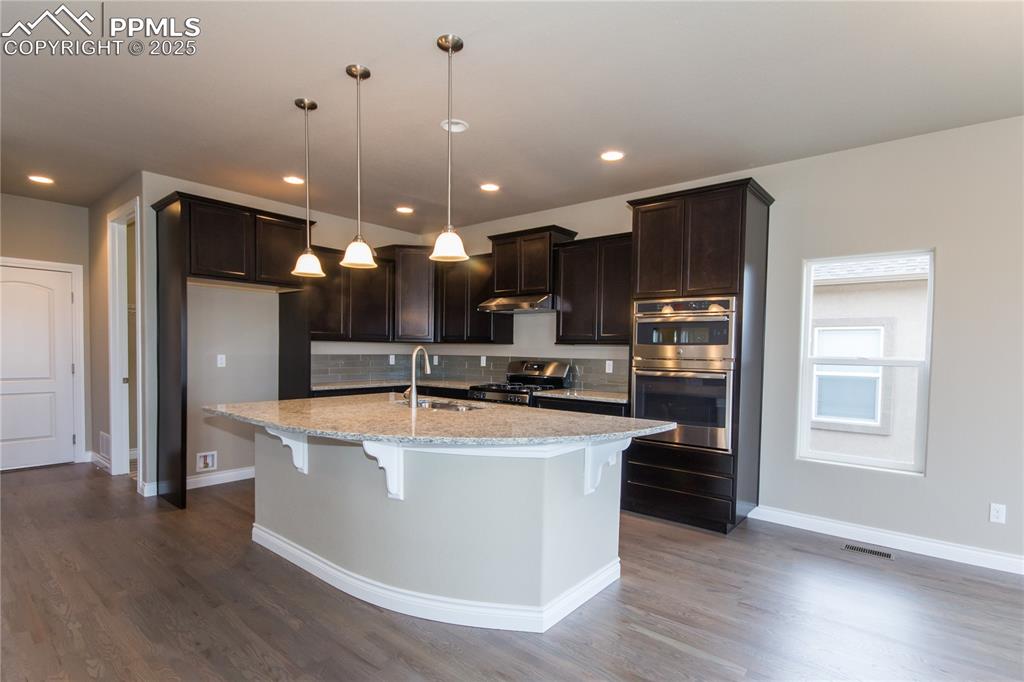 Image 7 of 28: Kitchen with dark wood finished floors, baseboards, dark brown cabinetry, a
