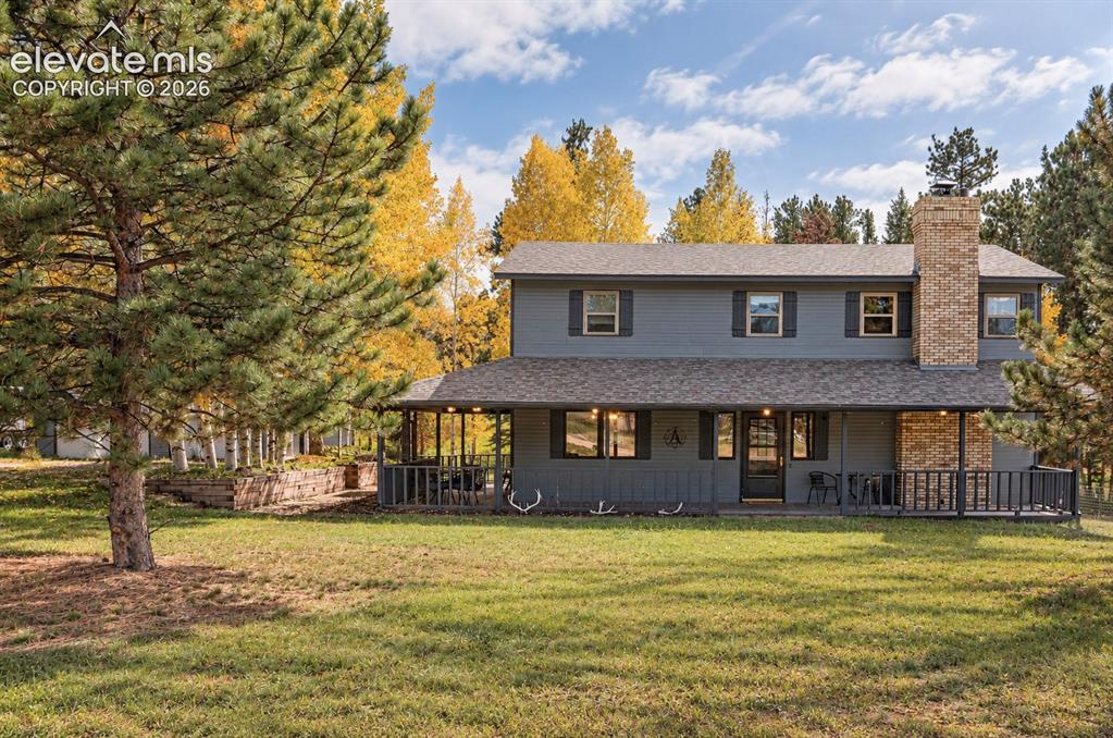 Caption: Two-story residential exterior with gray siding, a covered porch, an attached brick chimney, and a l