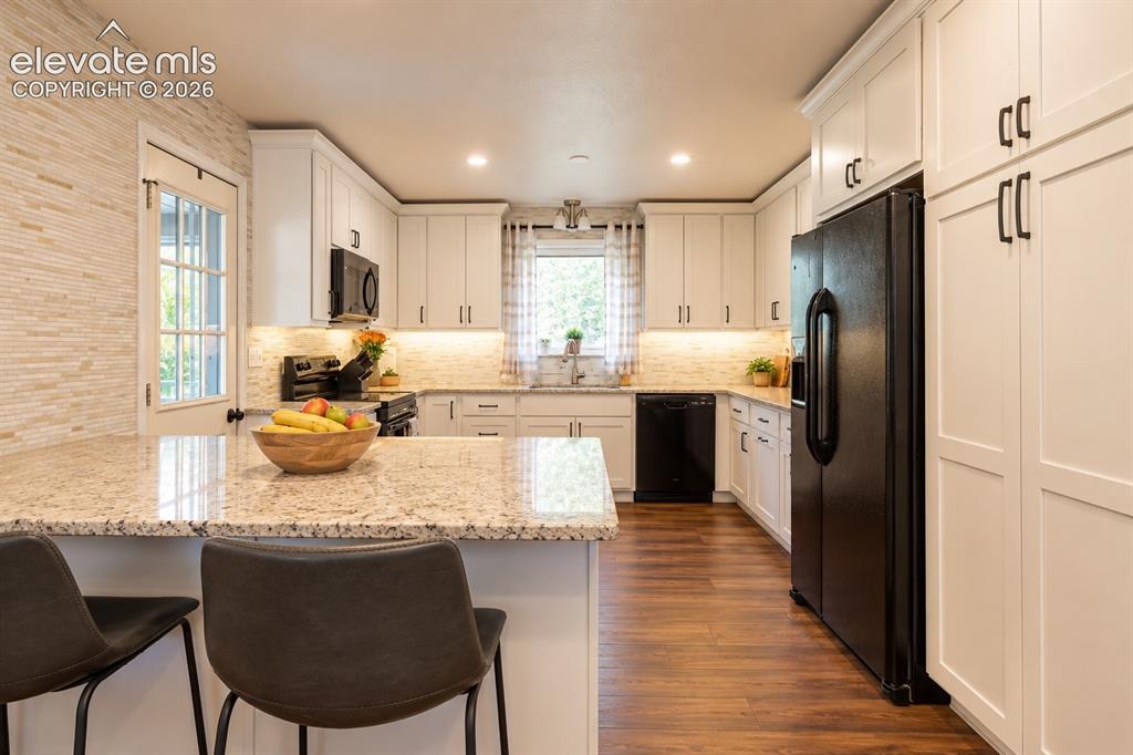 Image 10 of 30: Kitchen featuring granite countertops, white cabinetry, integrated applianc