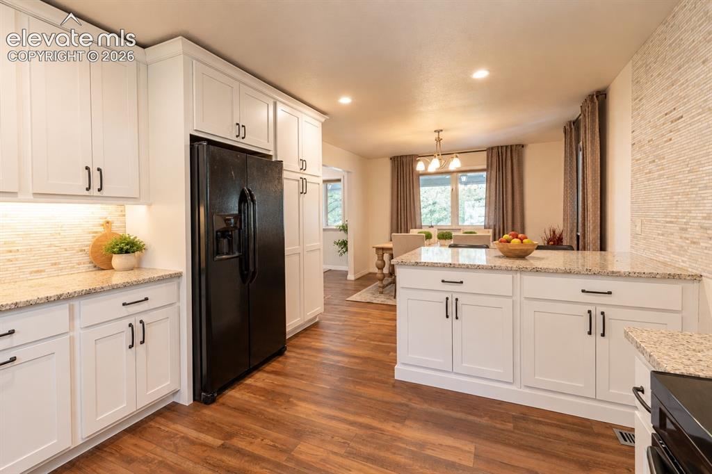 Image 12 of 30: Kitchen featuring white cabinetry, granite countertops, wood-finish floorin