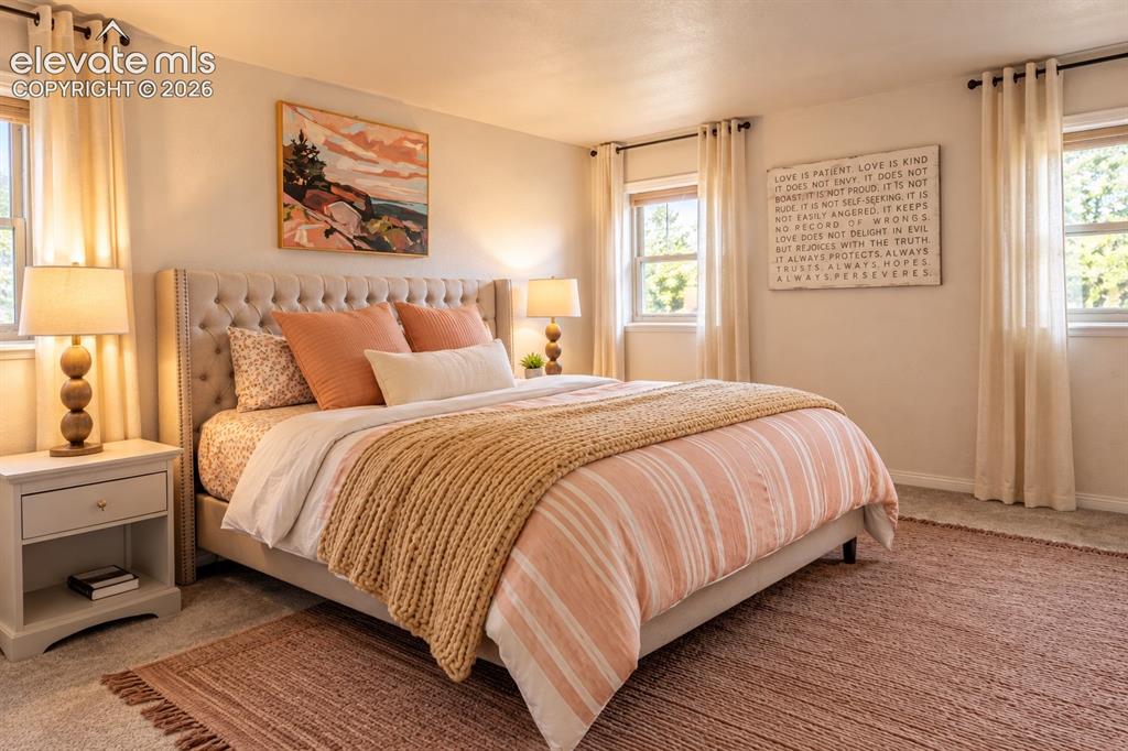 Image 13 of 30: Tufted upholstered headboard, multiple windows, soft wall-to-wall carpeting