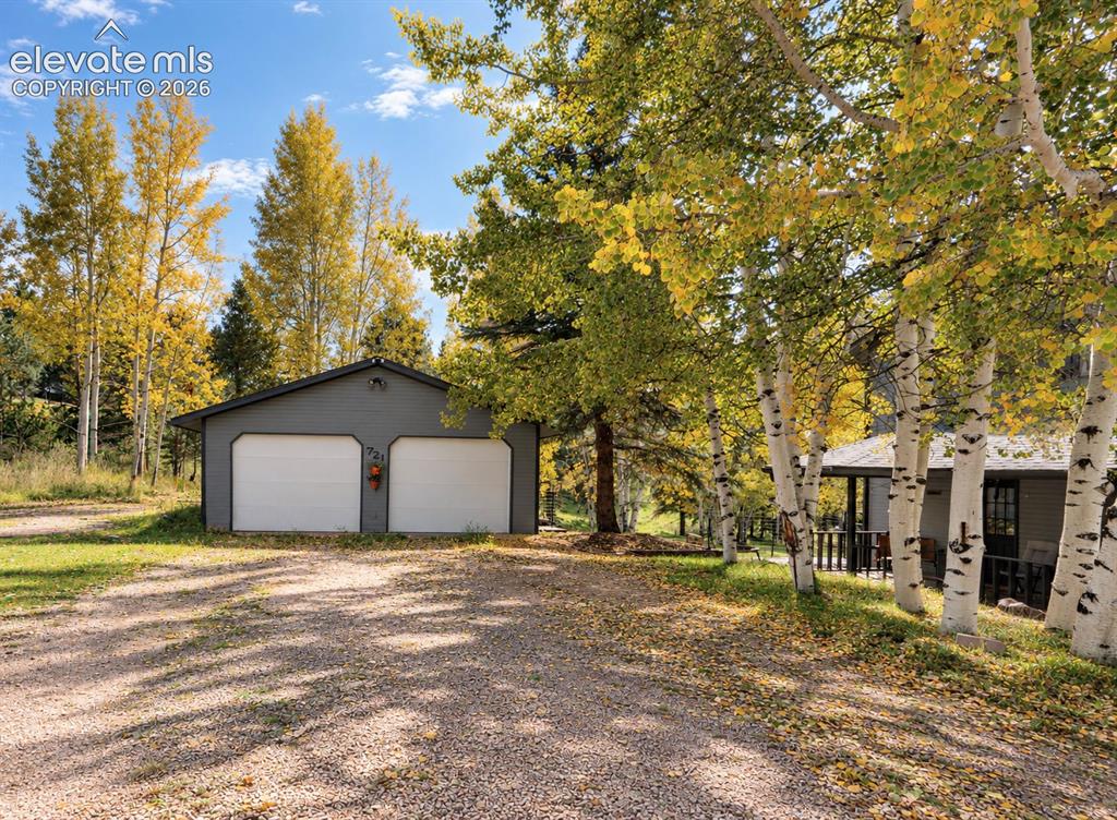 Image 27 of 30: Detached two-car garage with white garage doors and gray siding, gravel dri