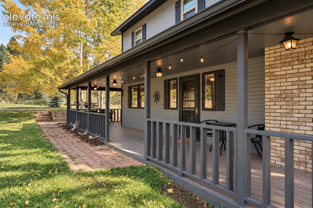 Image 29 of 30: Expansive covered porch with a wood-finish deck, brick accent siding, and c