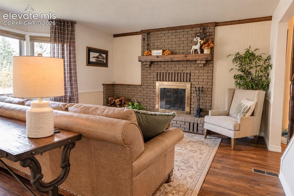 Image 3 of 30: Brick fireplace with a wood mantle, wood-finish flooring, and bay windows
