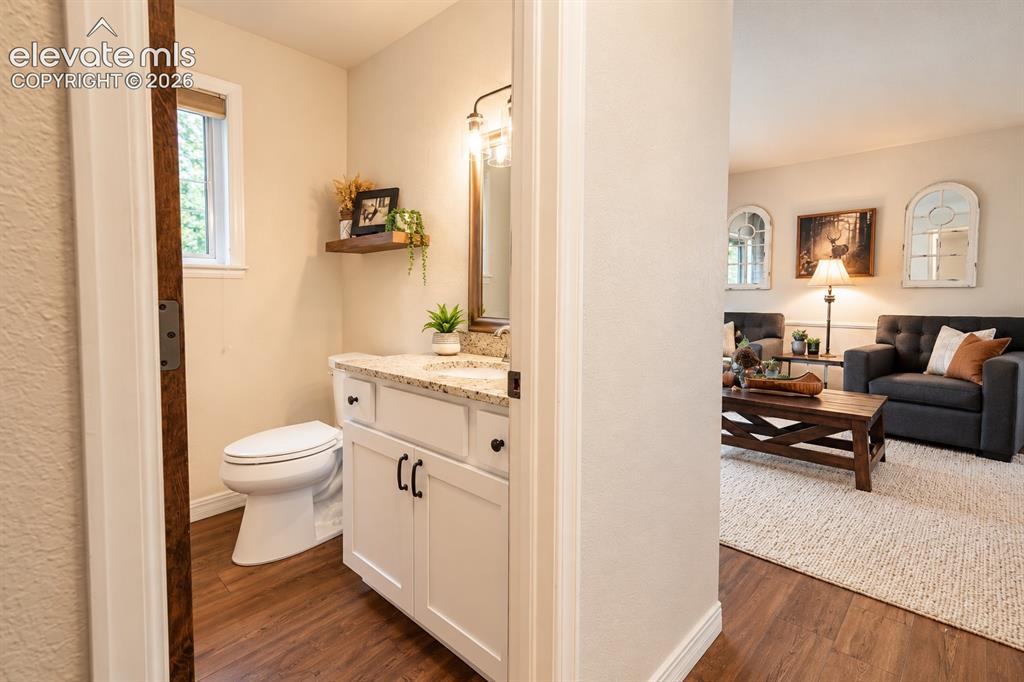 Image 7 of 30: Powder room featuring a white vanity with granite-finish countertop, wood-f