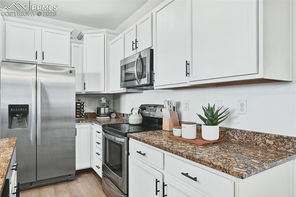 Image 8 of 25: Kitchen featuring stainless steel appliances, white cabinetry, light wood f