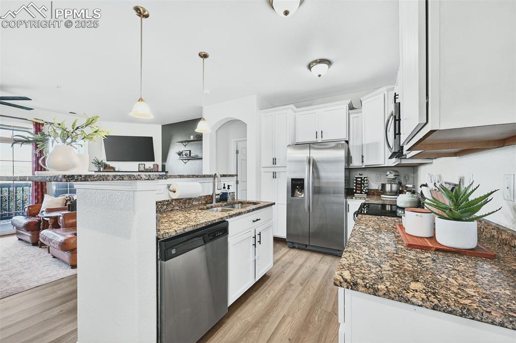 Image 9 of 25: Kitchen with dark stone counters, stainless steel appliances, hanging light
