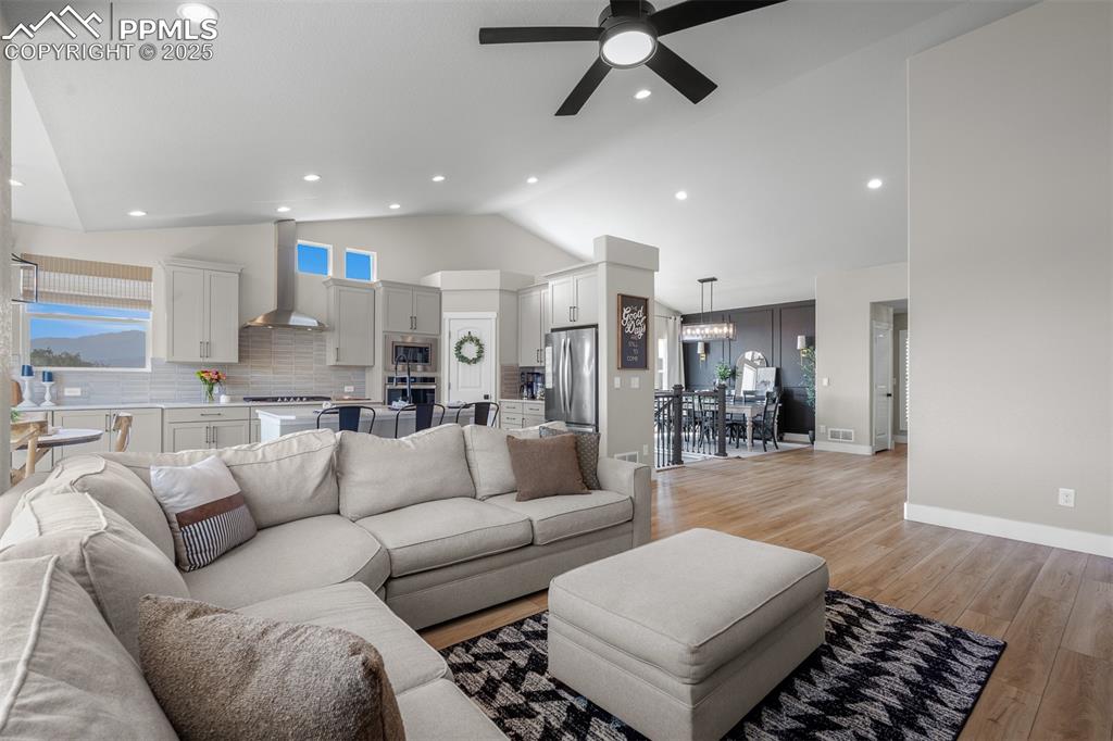 Image 11 of 37: Living room with vaulted ceiling, light wood finished floors, ceiling fan,