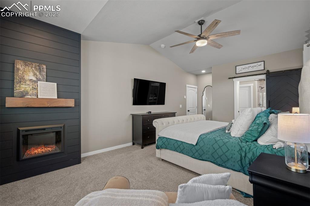 Image 18 of 37: Bedroom featuring a barn door, lofted ceiling, carpet floors, a fireplace,