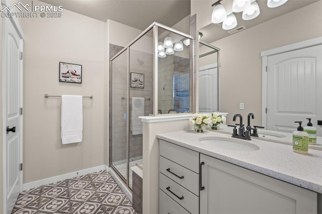 Image 33 of 37: Bathroom with vanity, a stall shower, tile patterned flooring, and a chande