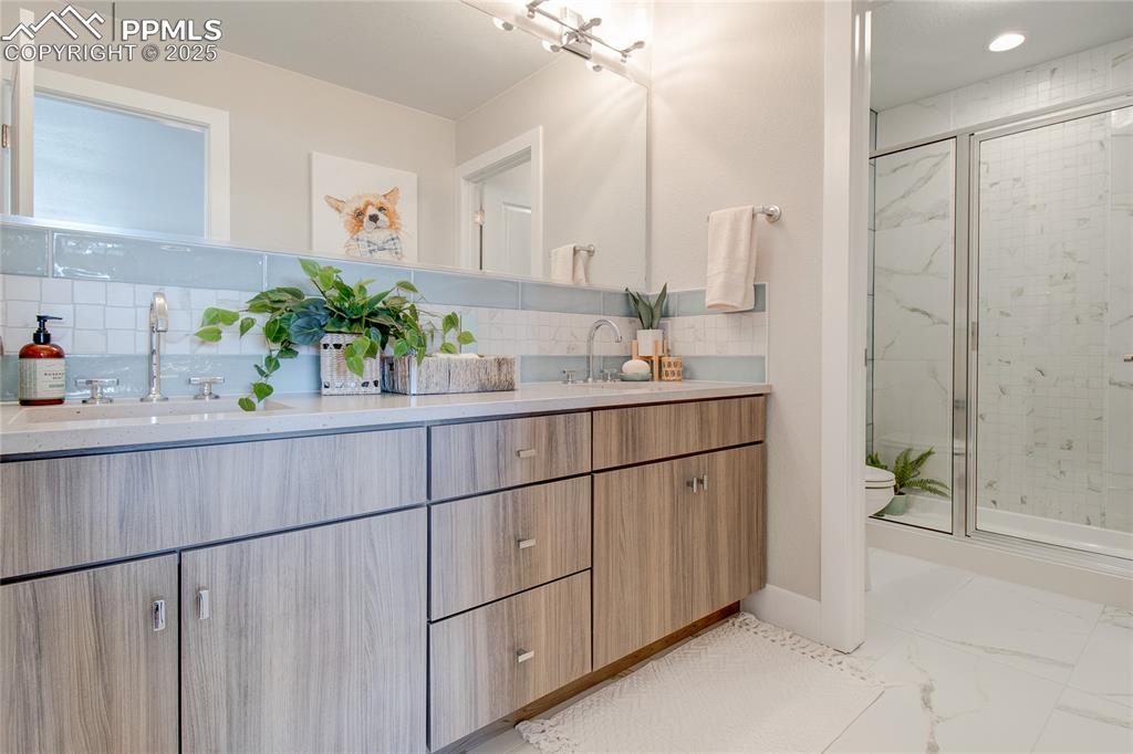 Image 20 of 29: Bathroom featuring backsplash, double vanity, a stall shower, marble finish