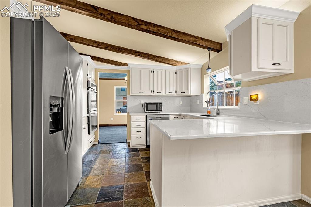 Image 13 of 50: Kitchen featuring stainless steel appliances, a peninsula, white cabinets,