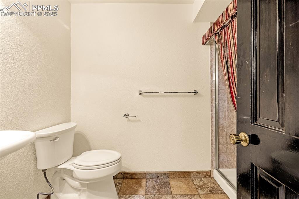 Image 26 of 50: Bathroom featuring a stall shower, a textured wall, and stone tile flooring