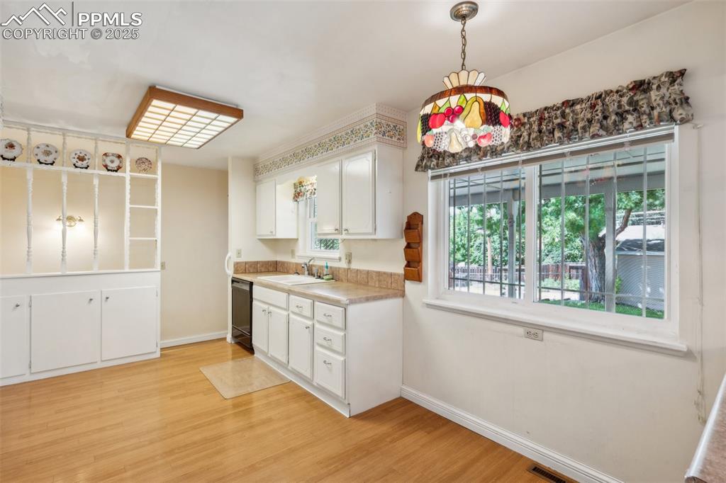 Image 12 of 30: Kitchen with black dishwasher, light wood-style floors, white cabinets, lig