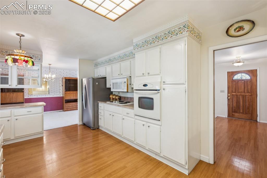 Image 13 of 30: Kitchen featuring white appliances, wallpapered walls, a chandelier, light