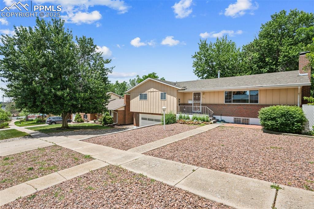 Image 2 of 30: Ranch-style house featuring driveway, brick siding, a chimney, board and ba