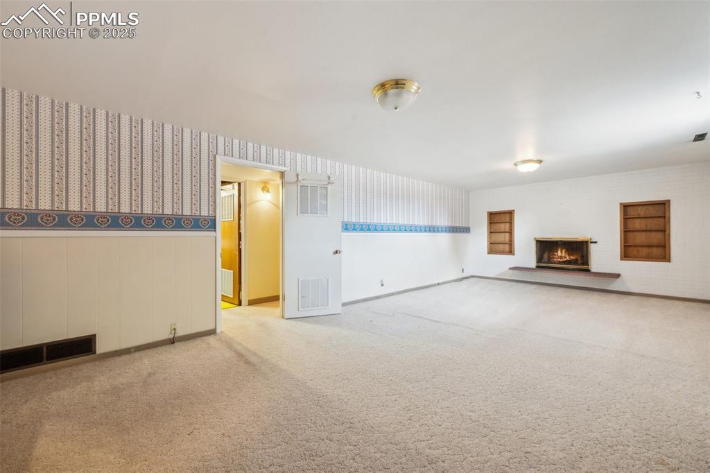 Image 25 of 30: Unfurnished living room featuring carpet floors, a lit fireplace, wainscoti