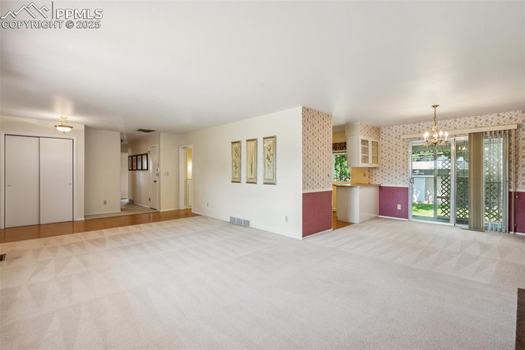 Image 7 of 30: Unfurnished living room featuring wallpapered walls, a chandelier, and ligh