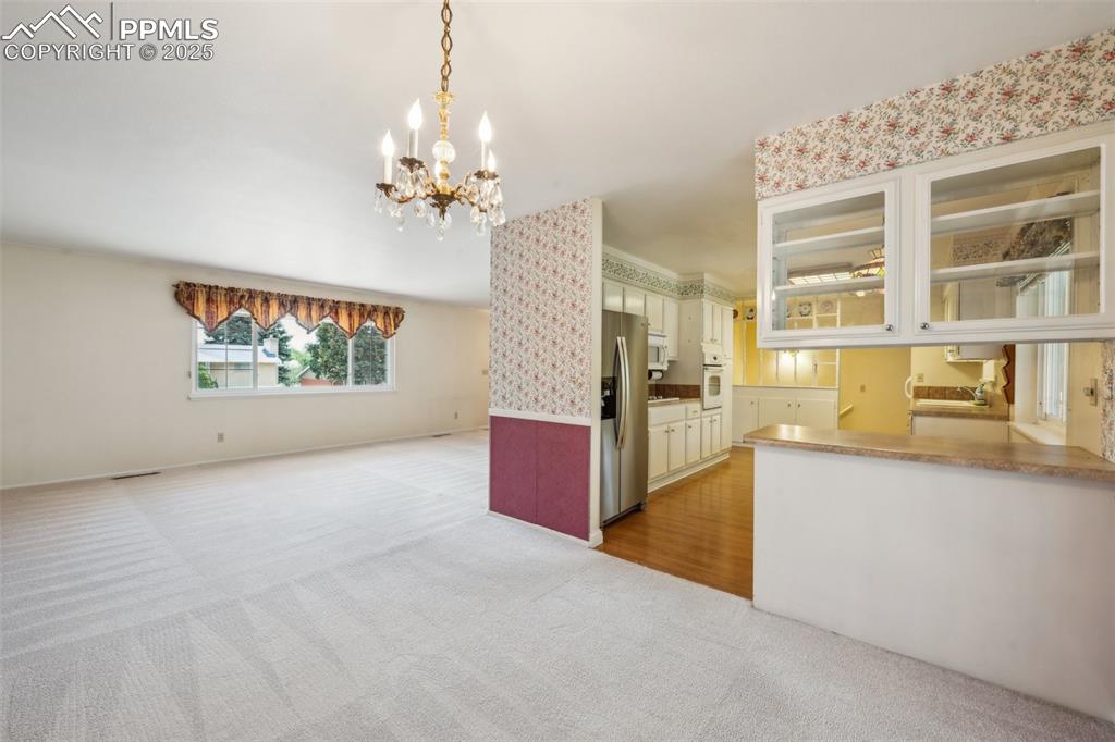 Image 8 of 30: Kitchen with oven, stainless steel fridge, light carpet, a chandelier, and