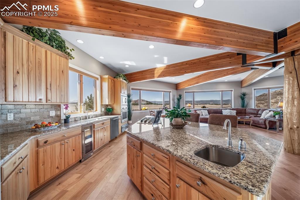 Image 11 of 50: Kitchen with an island with sink, light wood-style floors, beamed ceiling, 
